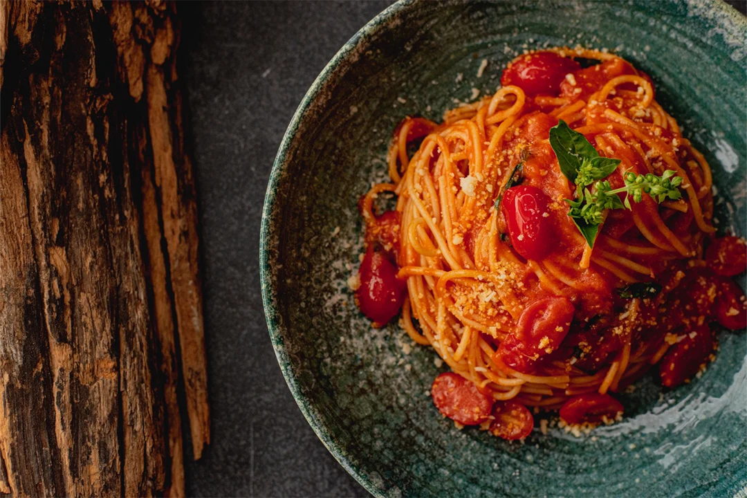 Spaghetti Al Pomodoro, um dos tipos de macarrão presentes na Mamma Jamma em prato de cerâmica sobre tampo escuro